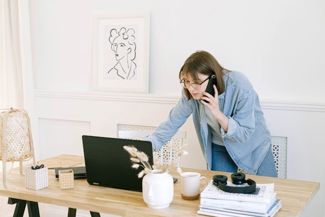 Person talking on the phone while using a laptop on a desk